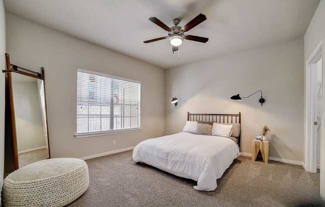 A bedroom with a bed, a ceiling fan, and a window with blinds.