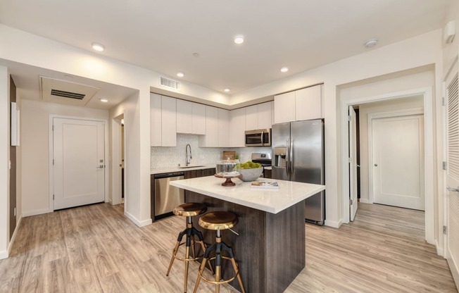 Kitchen with hardwood inspired floors and large island counter with two stools at Morgan Ranch Apartments, California