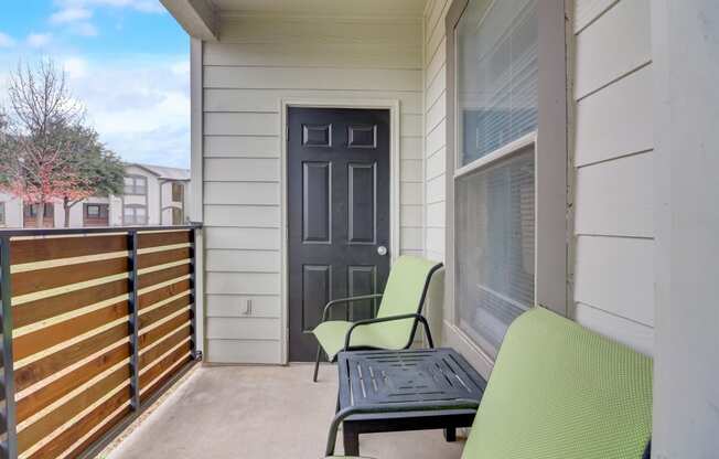 the front porch of a condo with two chairs and a table and a black door