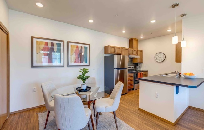 a dining area with a glass table and chairs and a kitchen in the background