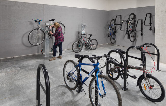 A woman is standing next to a bike in a room with several bikes on the wall. at Ravello Apartments, Redmond, WA