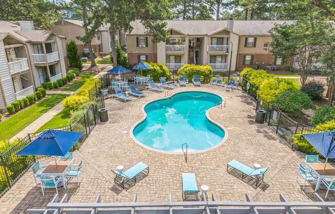 A swimming pool surrounded by chairs and umbrellas in a residential area.