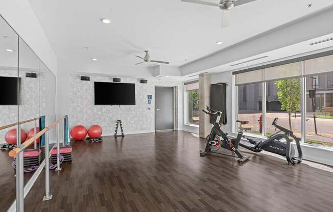 A spacious room with a wooden floor, a mirror, a fan, and exercise equipment.