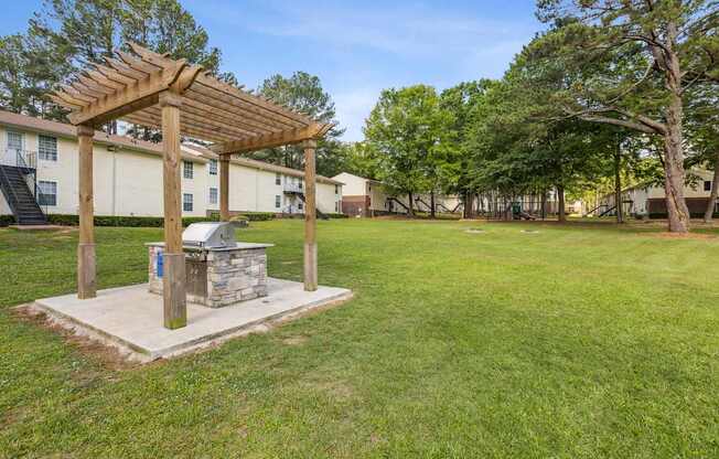 A wooden pergola is over a stone fireplace in a grassy area.