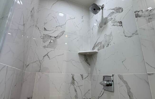 A shower area with a marble tile wall and a shower head.