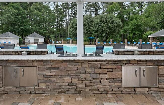 an outdoor kitchen with a pool in the background at Trails at Short Pump Apartments, Virginia,23233