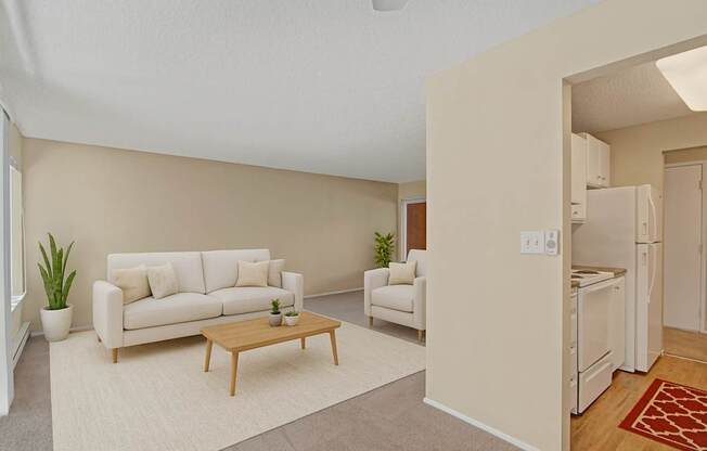 A bright living room here at Watercrest with soft carpet, neutral walls, and a large window, featuring comfortable seating, a wooden coffee table, and an adjacent kitchen with white appliances, creating an open and inviting layout.