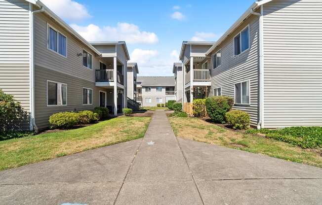 a pathway between two apartment buildings with grass and bushes