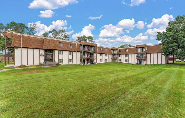A large grassy field in front of a building with a blue sky and white clouds.