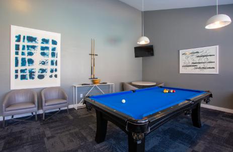 A pool table is in the middle of a room with two chairs and a painting on the wall.