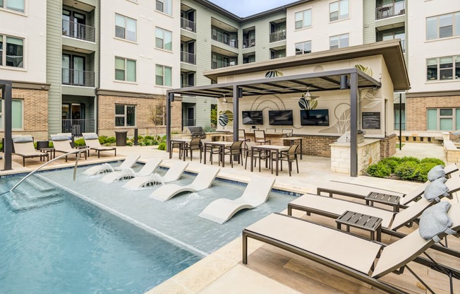 a swimming pool with lounge chairs and tables in front of an apartment building