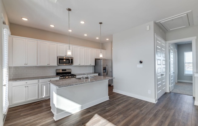 Rental Homes in Houston, TX - East Heights - Kitchen with Vinyl Plank Flooring, White Cabinetry, Stainless Steel Appliances, Granite Countertops, Kitchen Island with Pendant Lights, and Tile Backsplash.