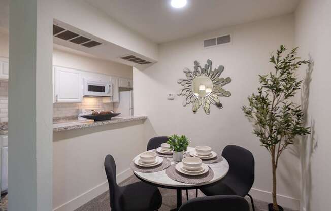 A dining area with a table set for four and a potted plant with a view of the kitchen pass-through window in a 1 bedroom, 1 bath 554 sq ft apartment home at The Biltmore Apartments located in the Vickery Midtown neighborhood of Dallas, TX.
