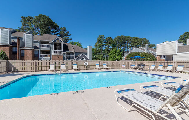 A swimming pool surrounded by lounge chairs and buildings in the background.