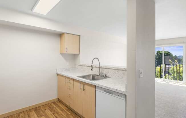 a kitchen with plank flooring, a sink, dishwasher, and natural light from the sliding glass doors at Guinevere Apartment Homes, Seattle, WA