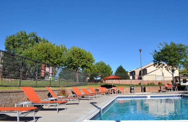 North Creek Apartments pool with orange lounge chairs and metal fence on the left and beige building in the background