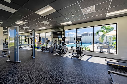 a gym with cardio equipment and windows overlooking a swimming pool the gym  at a residential apartment community Resia in Decatur GA