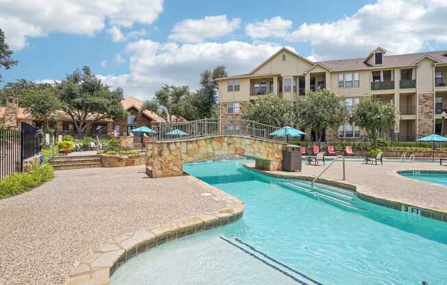 a swimming pool with a stone bridge over it next to an apartment building at The Verandah, Austin, TX, 78726