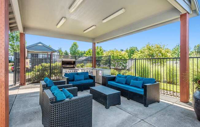 A patio with a black wicker sofa and blue cushions in front of a BBQ grill at The Landing Apartments and Townhomes, Oregon, 97045