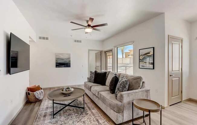 A living room with a grey couch, a coffee table, and a flat screen TV mounted on the wall.