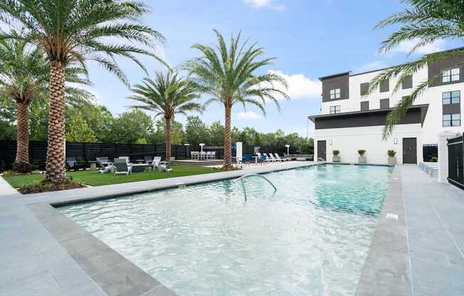 A swimming pool surrounded by palm trees and an apartment building in the background.