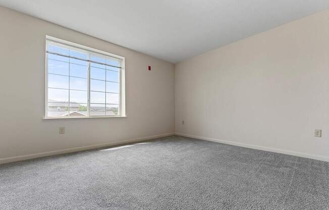 A bedroom with a large window and carpeted floor at Fieldstream Apartment Homes in IA 50023