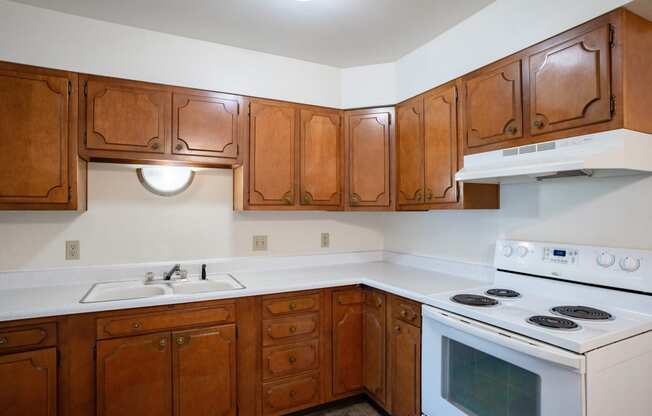 an empty kitchen with wooden cabinets and white appliances.  Fargo, ND Crown Court 1 Apartments