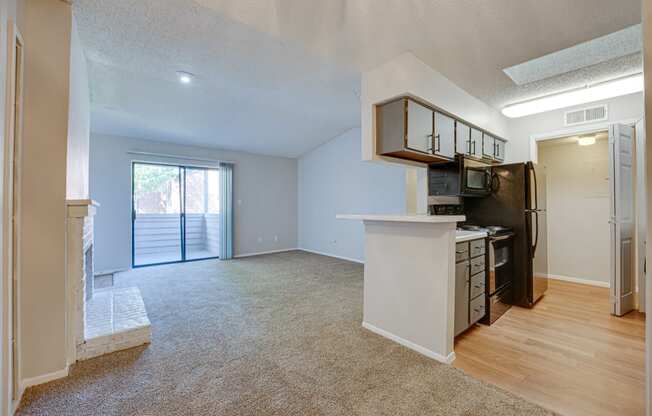 an empty living room with a kitchen and a door to a balcony