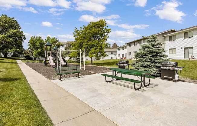 A playground with a slide, swings, and a picnic table in a park.