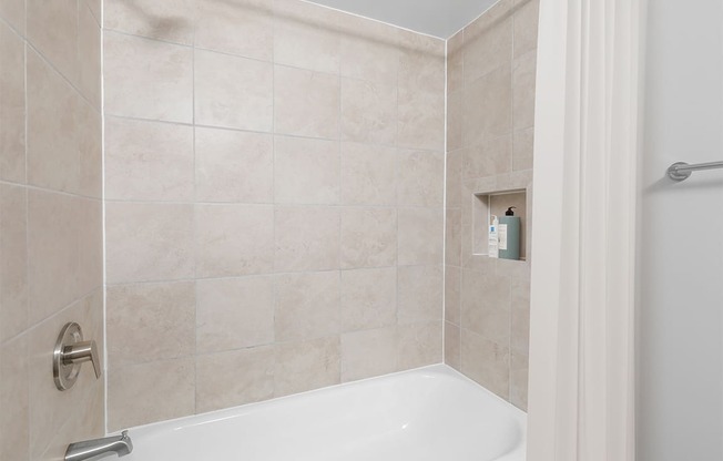 a bathroom with beige tiles and a white bathtub at Padonia Village Apartments, Timonium MD