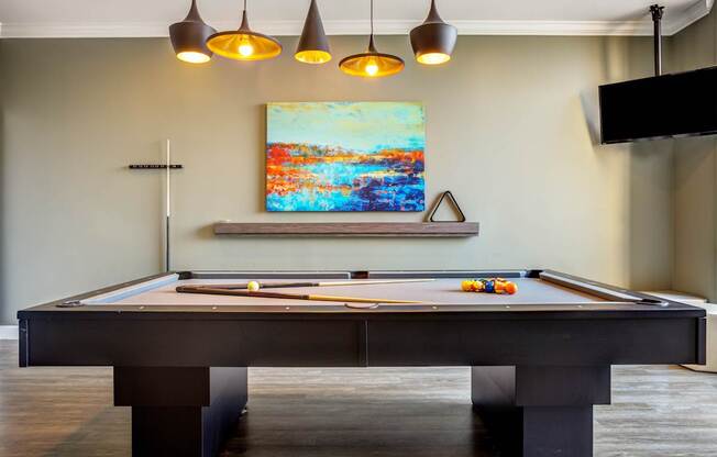 A pool table with a painting hanging above it.