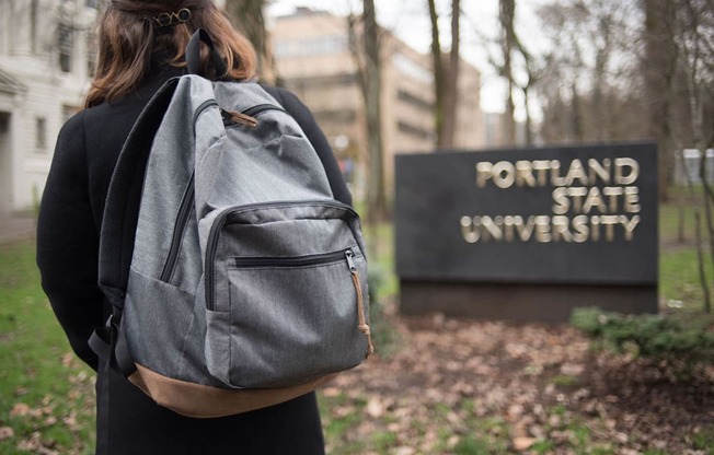 a woman with a backpack standing in front of the fountain state university sign