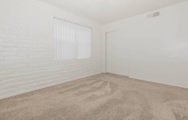 A room with a carpeted floor and a window with blinds.
