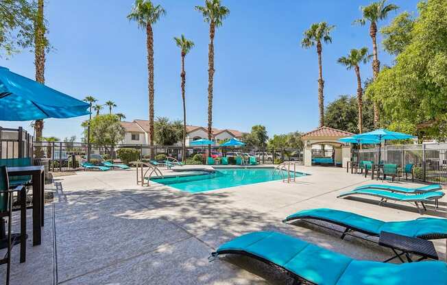A pool surrounded by palm trees and blue umbrellas.