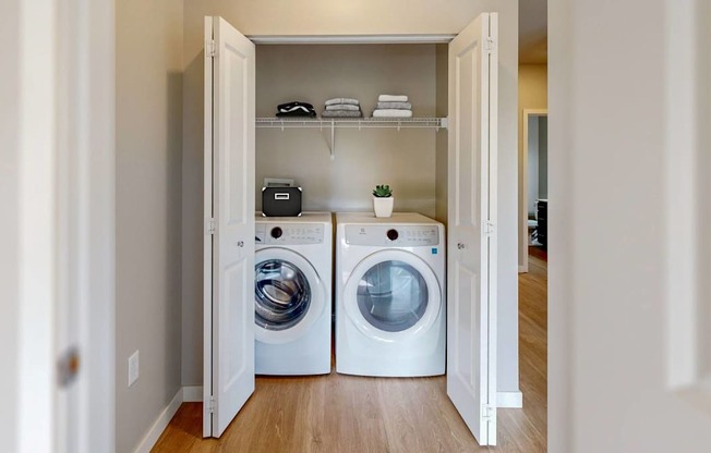 A laundry room with two washing machines and a shelf with towels and a plant.