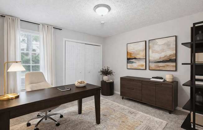 A room with a desk, chair, and two paintings on the wall.