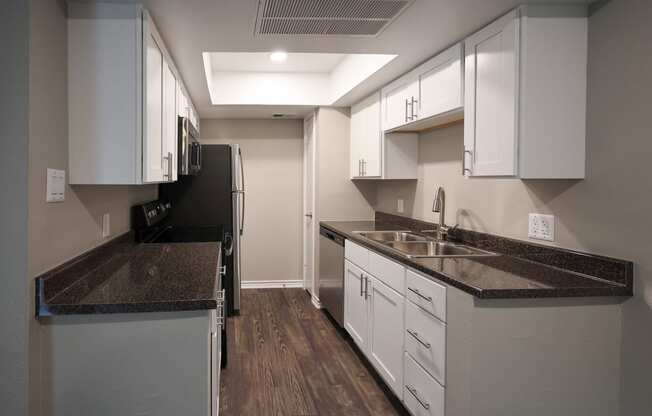 View of kitchen with whit cabinets, stainless appliances, dark counters, and wood look floorin