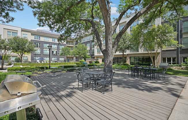 A wooden deck with a grill and chairs is surrounded by trees.