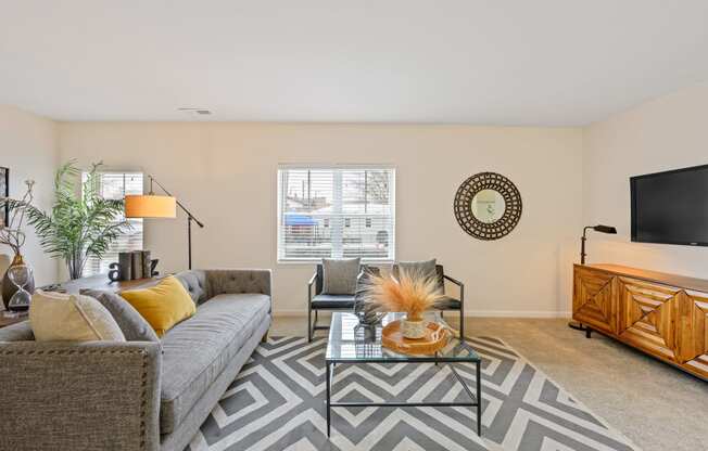 a living room with a gray couch and a glass coffee table on a chevron rug