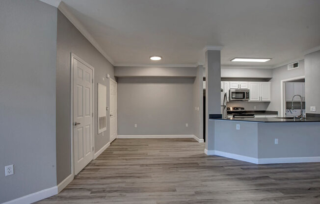 an empty room with a kitchen in the background