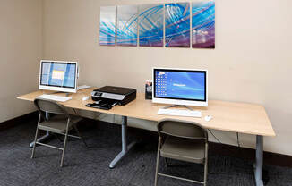 two computers and a printer sit on a table in a room with two paintings on the wall