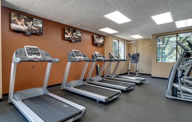 Fitness center with a row of treadmils and TVs on the wall