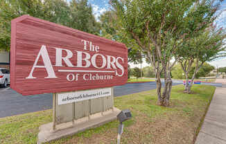 A sign that says "The Arbors of Cleburne" is in front of some trees.