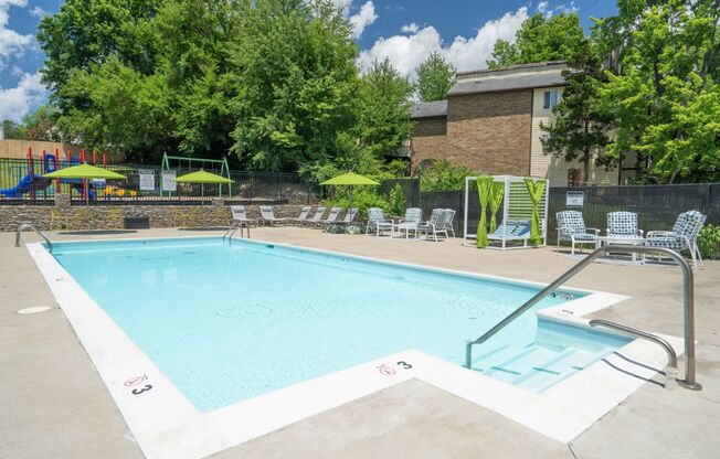 a swimming pool with lounge chairs and umbrellas in front of a brick building at Stonewater Apartments, Louisville Kentucky