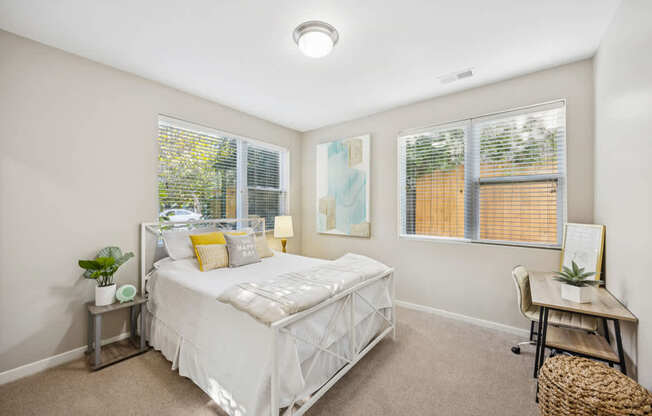 A bedroom with a white bed and a window with blinds.