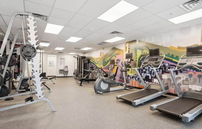 a gym with cardio equipment and a wall with graffiti