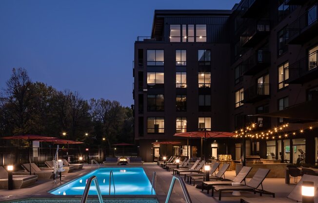 Dusk view of hot tub, pool, and pool seating on terrace with lit apartment windows