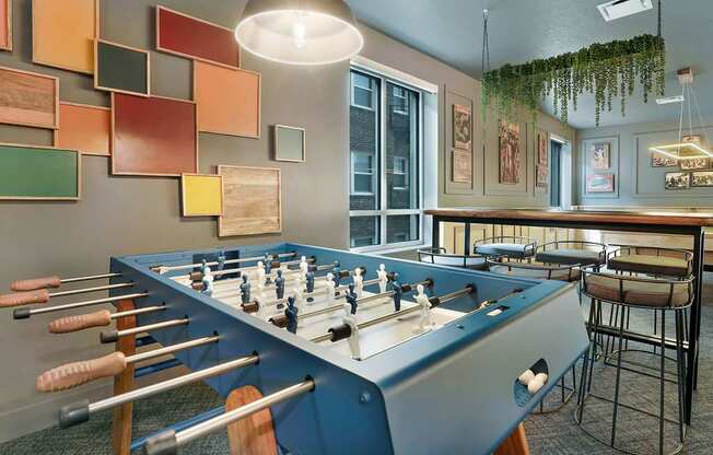 A foosball table is in the middle of a room with a blue wall and a green plant hanging from the ceiling.