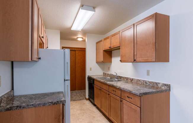 a kitchen with wood cabinets and granite counter tops and a refrigerator. Fargo, ND Schrock Apartments