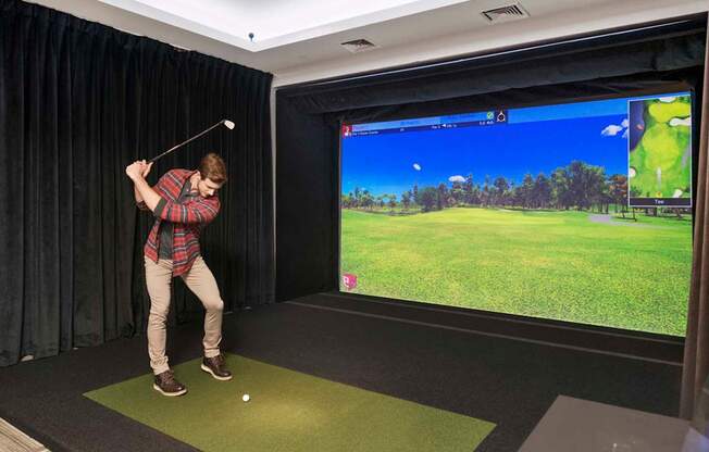A man is playing golf in a room with a large screen showing a golf course.